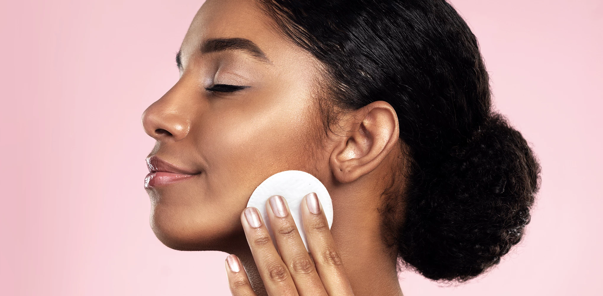 Smilende person med lukkede øyne som bruker en bomullspad for å rense ansiktet