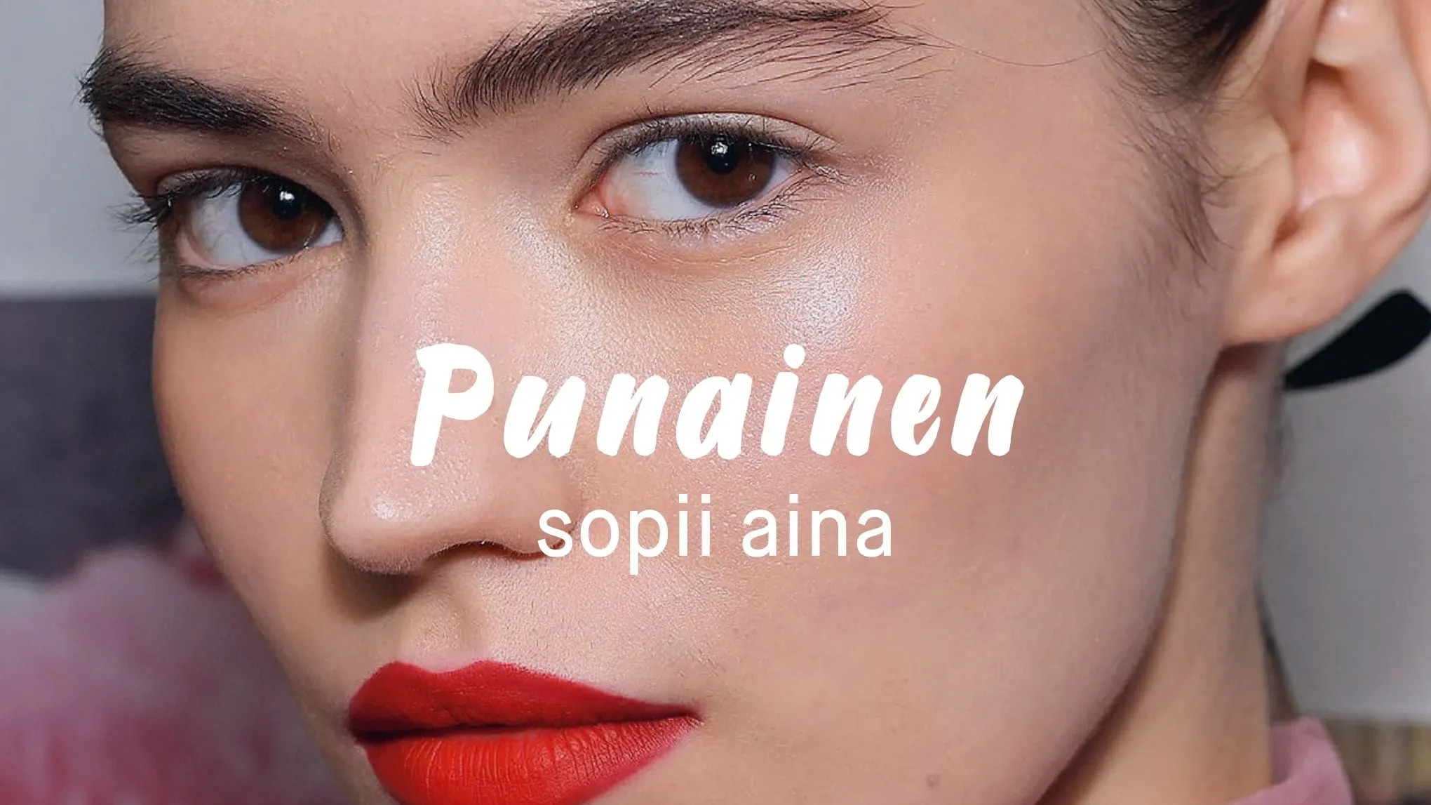 Nainen, jolla on meikkiä ja punaiset huulet, hiukset kiinni ja katsoo suoraan kameraan.