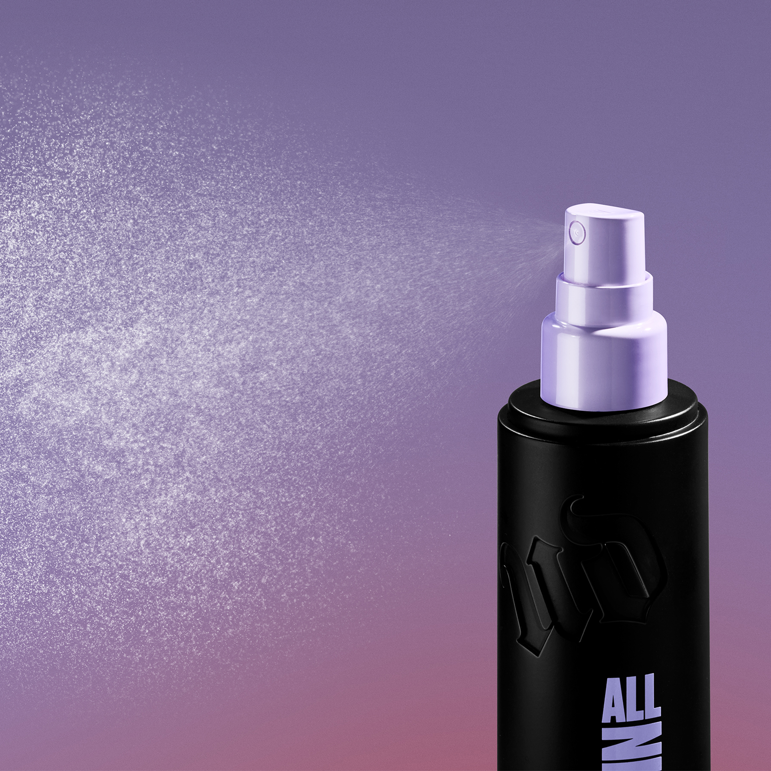 Urban Decay All Nighter setting spray i svart flaske med lilla spraypumpe som sprayer en fin mist mot lilla bakgrunn. På flasken vises teksten “ALL NIGHTER”.