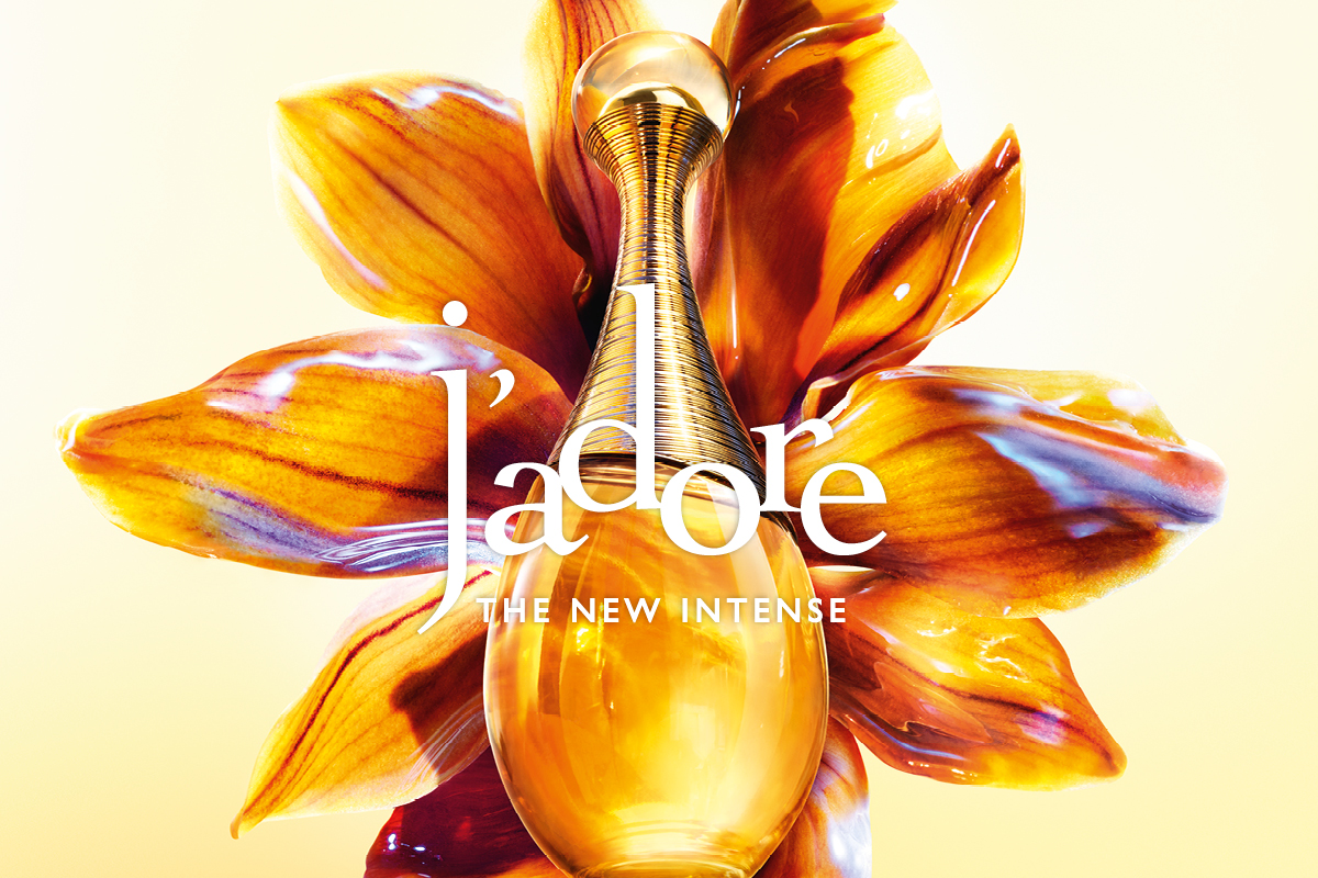 Dior J’adore -hajuvesipullo kullan sävyssä suuren oranssin ja keltaisen sävyisen kukan edessä, jossa on kiiltävä pinta. Kuvassa teksti: "J’adore" ja "THE NEW INTENSE".