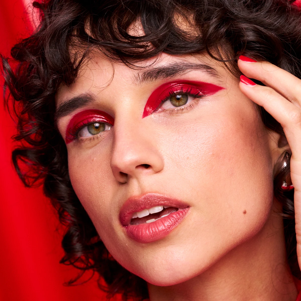 Kvinna med kort lockigt hår, röd ögonskugga mot röd bakgrund