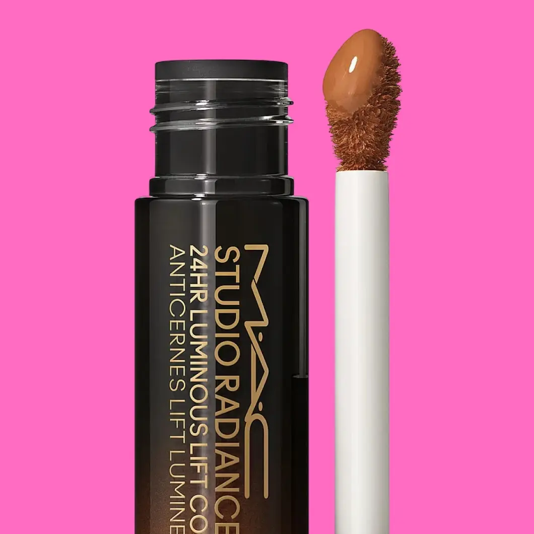 MAC Studio Radiance 24HR Luminous Lift Concealer i svart emballasje med applikator og brun concealer mot en rosa bakgrunn. Teksten «MAC Studio Radiance 24HR Luminous Lift Concealer» er synlig på emballasjen.