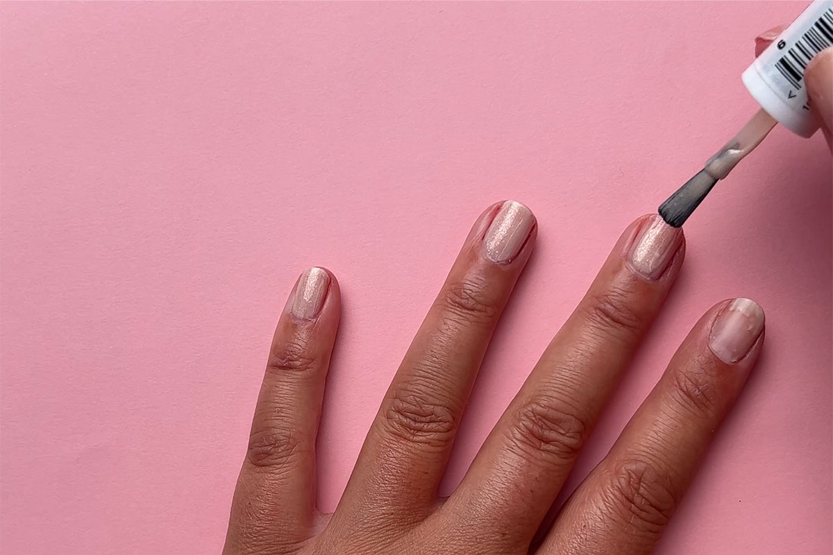 Nagellack som appliceras på en nagel mot en rosa bakgrund
