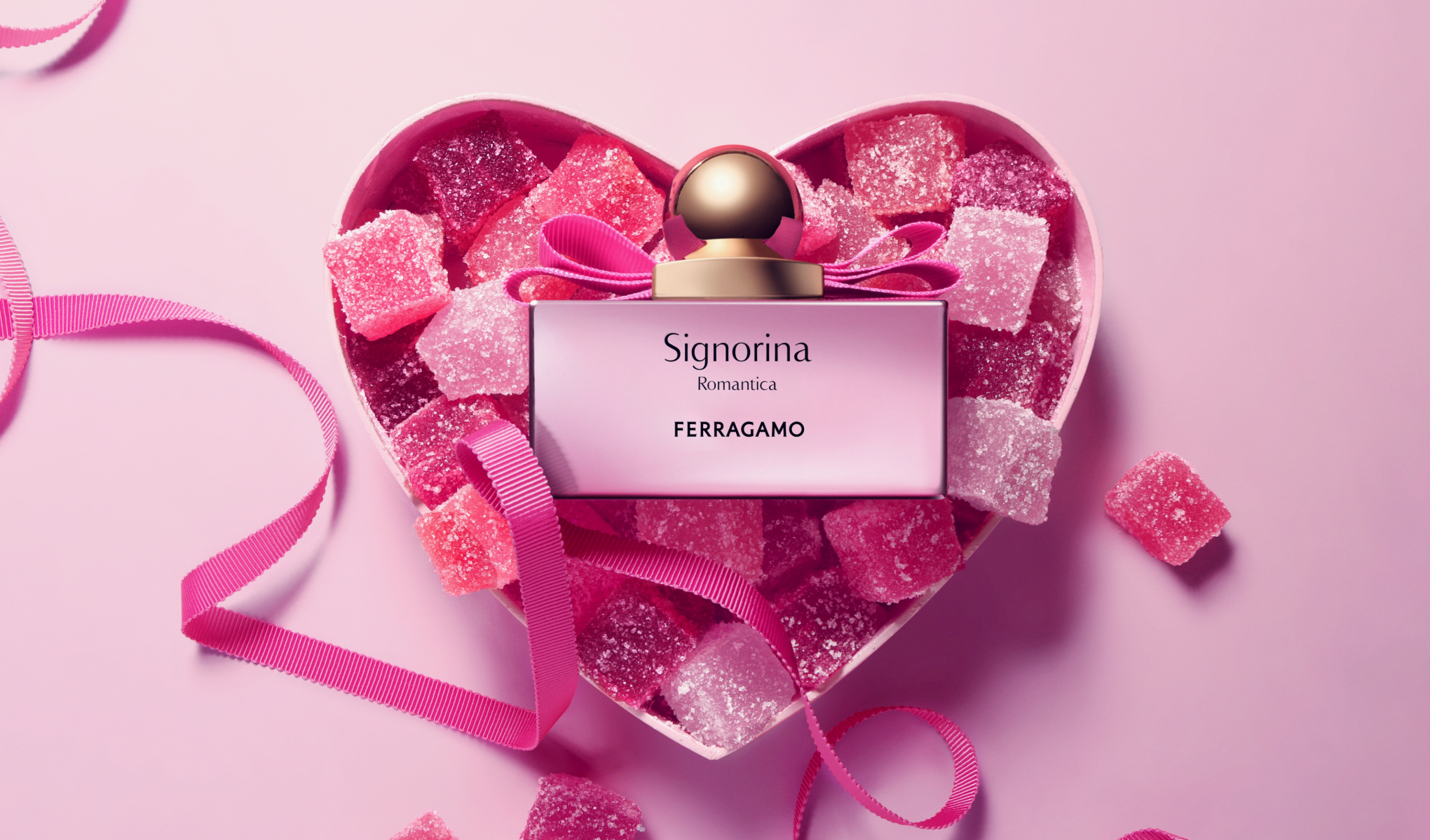 Ferragamo Signorina Romantica -hajuvesipullo sydämenmuotoisessa rasiassa, joka on täynnä vaaleanpunaisia hyytelökarkkeja vaaleanpunaista taustaa vasten. Näkyvä teksti sisältää “Signorina Romantica” ja “FERRAGAMO”.