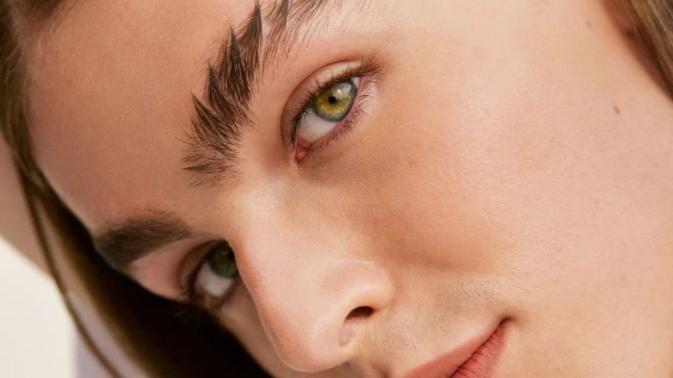 Människoansikte med gröna ögon, välvårdade ögonbryn och naturlig makeup.