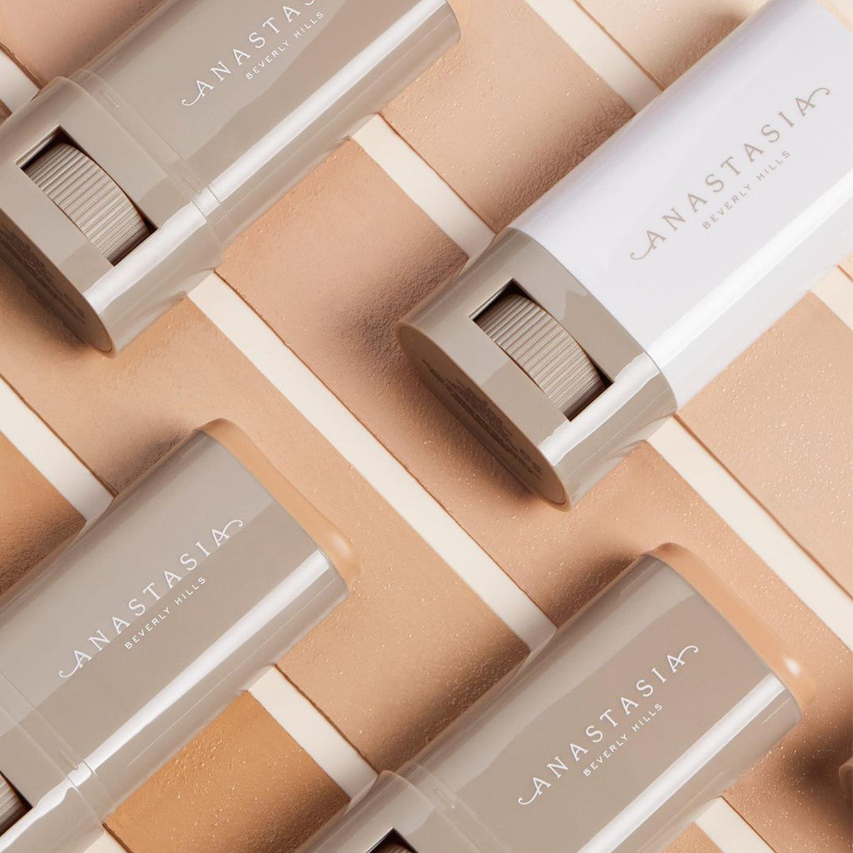 Anastasia Beverly Hills -merkin meikkikynä. Kynät on sijoitettu vinosti taustalle, jossa on eri ihonvärejä edustavia beigen ja ruskean eri sävyjä. Jokaisella kynällä on harmaa ja valkoinen pakkaus, jonka kylkeen on painettu tuotemerkin nimi. Taustalla on kuvioitu pinta, joka korostaa tuotteita ja niiden värejä.