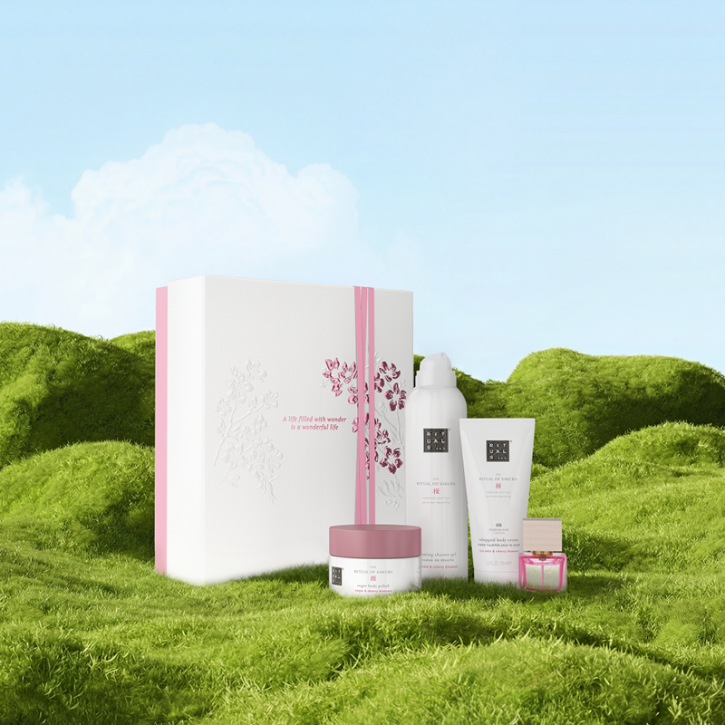 Rituals gaveeske som inneholder dusjgel, kroppskrem, håndkrem og duftlys på grønt gress med blå himmel i bakgrunnen.