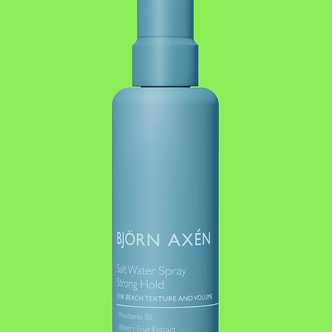 Flaske merket “BJÖRN AXÉN Salt Water Spray Strong Hold For Beach Texture and Volume ProVitamin B5 Bilberry Fruit Extract” mot grønn bakgrunn.