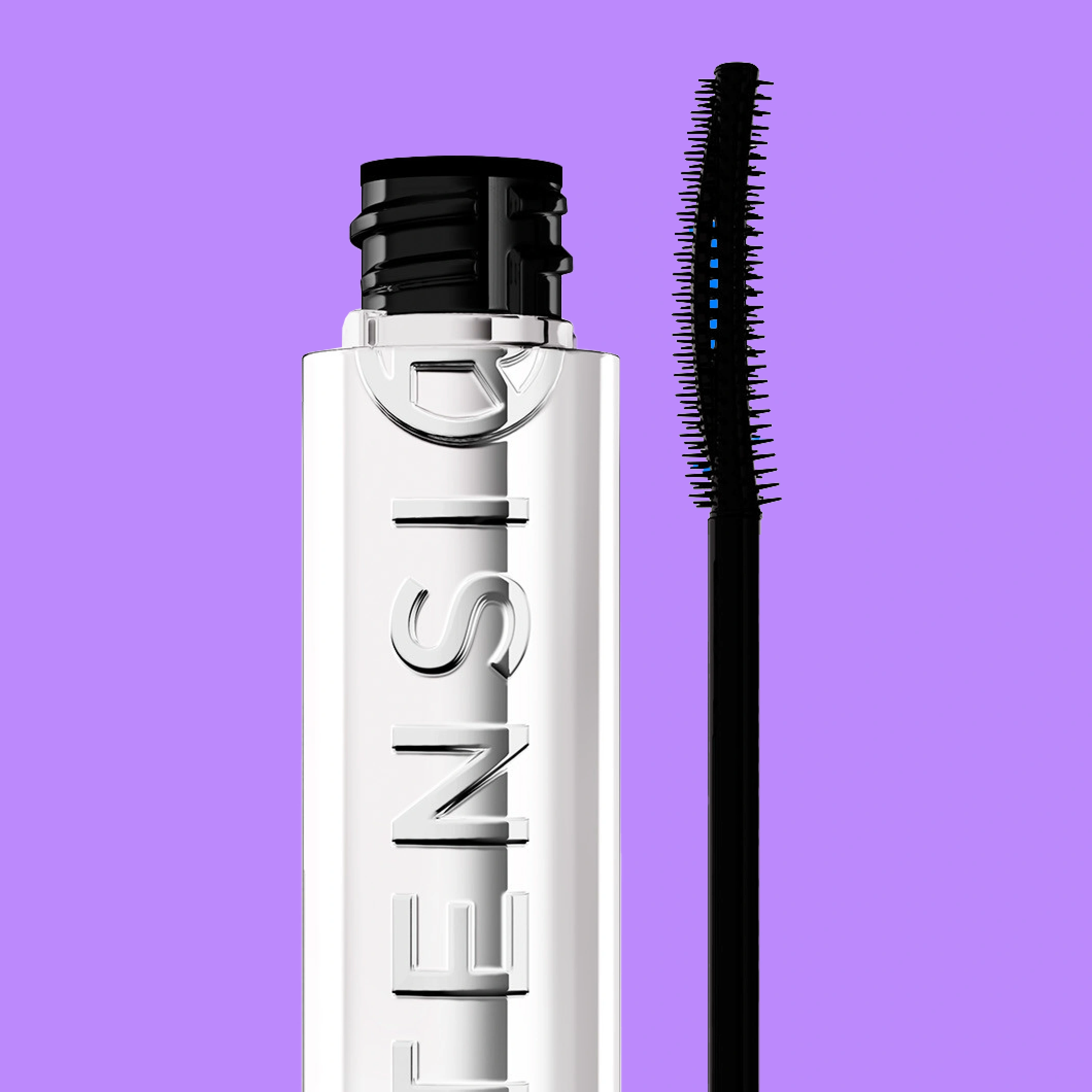 Lähikuva valkoisesta ripsiväristä ja erillisestä mustasta harjasta sekä hohtavasta ruskeasta luomivärikynästä violettia taustaa vasten. Metalli- ja muovipakkaukset selkeästi esillä.