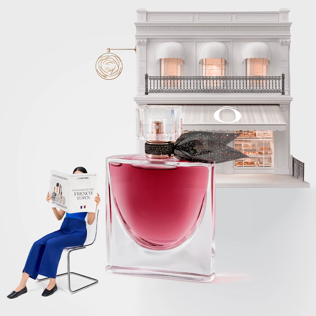 En kvinne i blå klær leser et magasin ved siden av en stor parfymeflaske med rosa væske. I bakgrunnen er en elegant bygning med balkong og butikkvinduer.