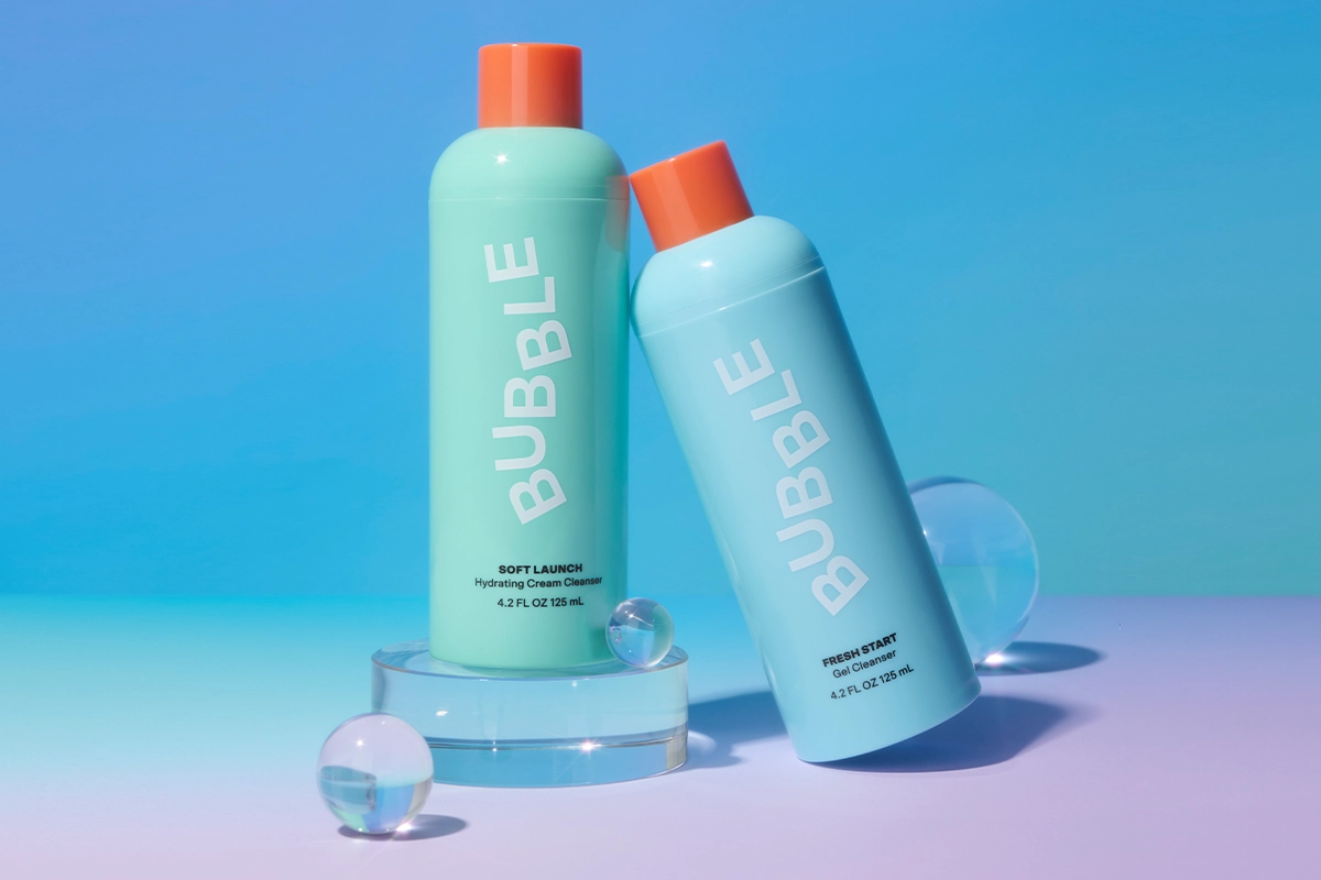 To Bubble-renseprodukter i mintgrønne og lyseblå flasker med oransje korker. Bakgrunnen er blå og lilla.