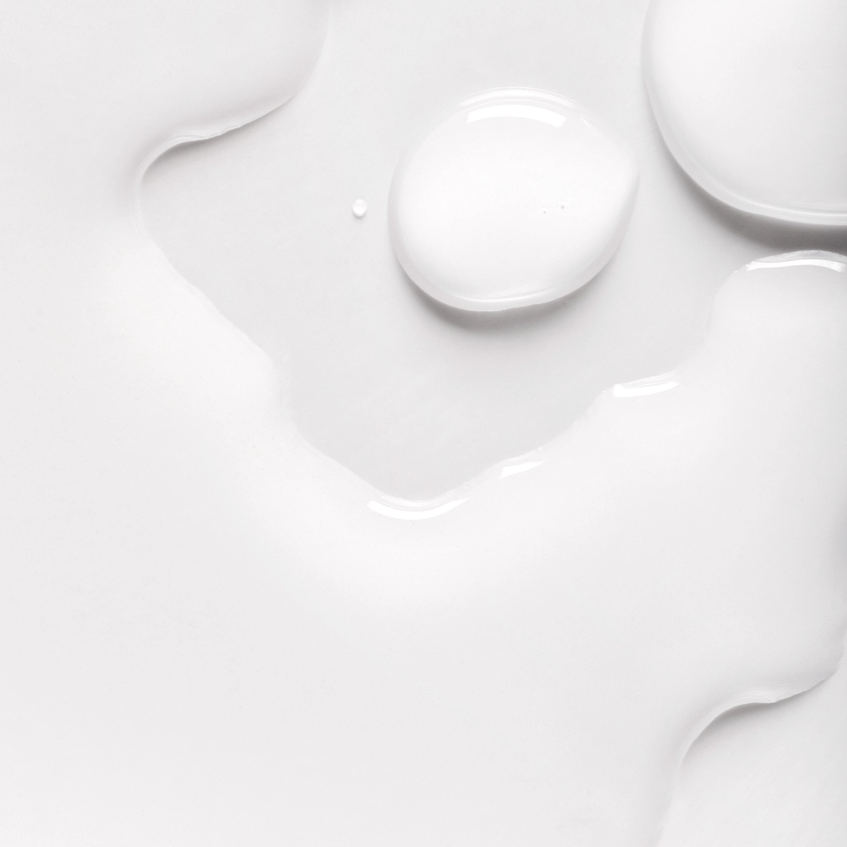 Lähikuva valkoisista nesteen pisaroista vaalealla pinnalla, pehmeitä muotoja ja heijastuksia.
