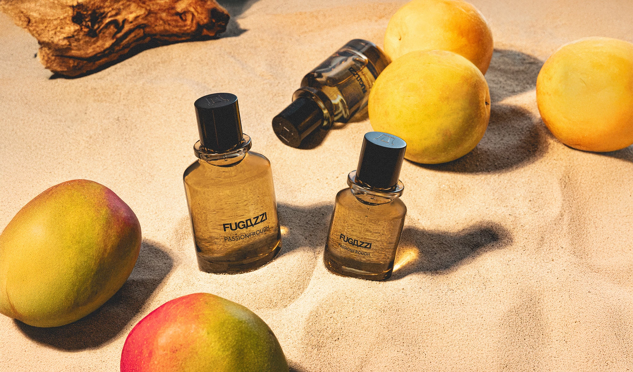 Tre produkter av Fugazzi placerade på en strand bland apelsiner och mangos samt en bit av en trästock i solljus.
