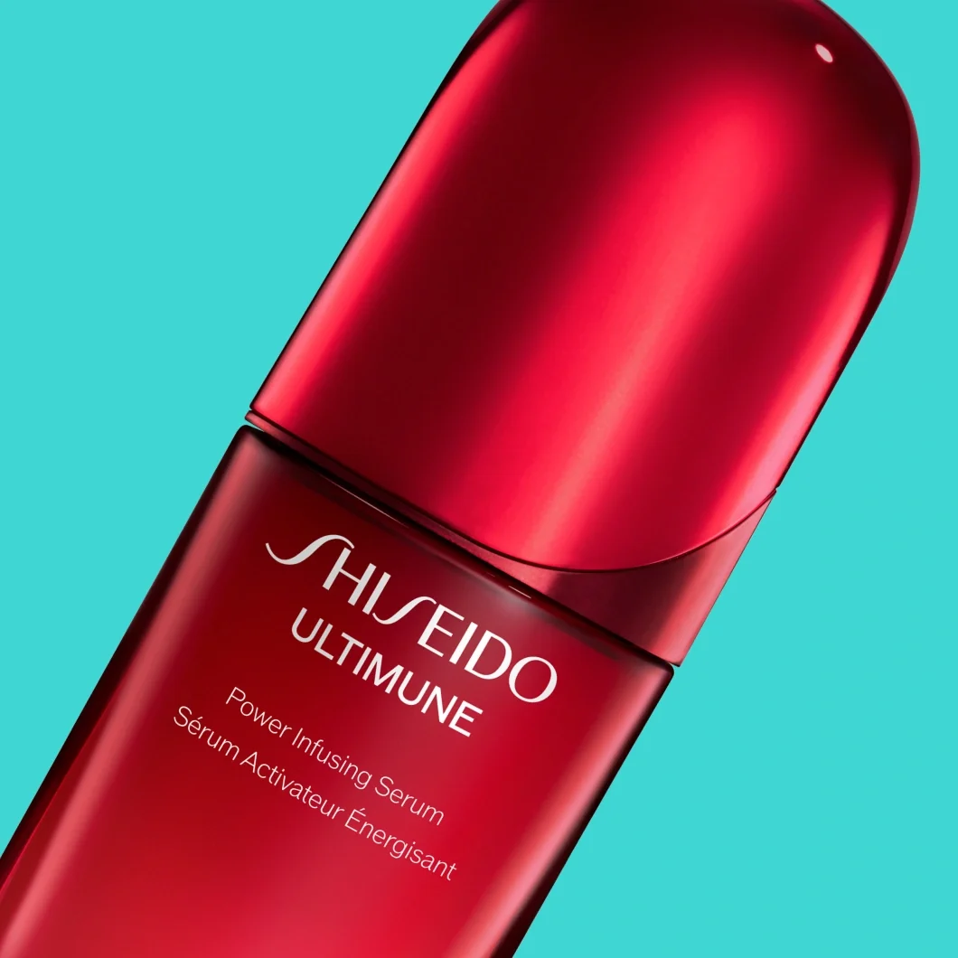 Shiseido Ultimune Power Infusing Serum i en röd flaska mot turkos bakgrund. På förpackningen syns texterna "SHISEIDO", "ULTIMUNE", "Power Infusing Serum" och "Sérum Activateur Énergisant".