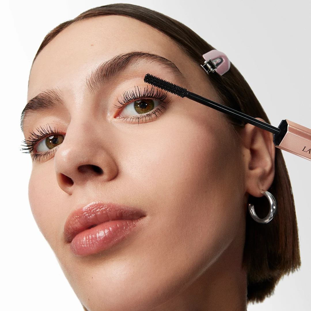 Närbild av en person som applicerar Lancôme mascara på övre fransar, med tydlig borste och öppnad hylsa nära ögat.