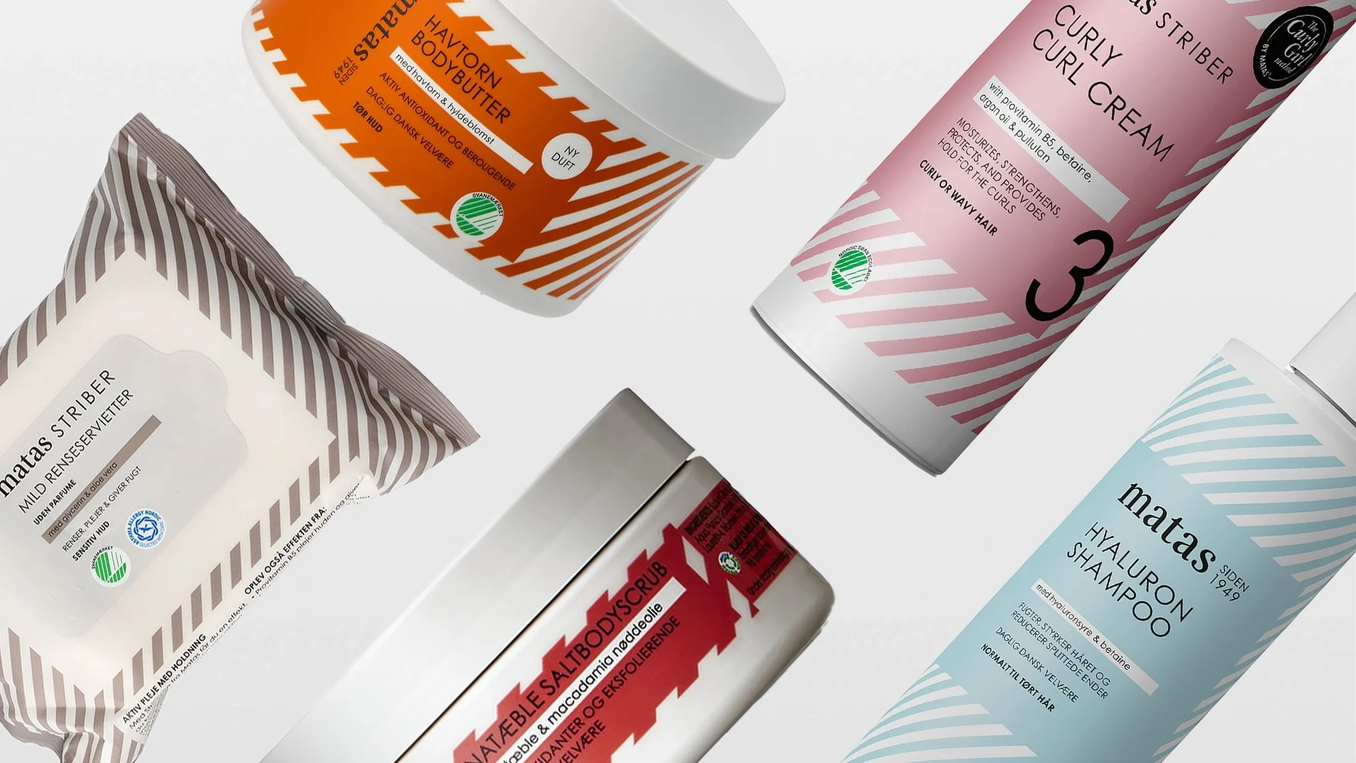 En samling av forskjellige skjønnhetsprodukter, inkludert en bodybutter, en curl cream, en hyaluronsjampo, en saltskrubb og ansiktsservietter. Produktene er stilfullt arrangert mot en hvit bakgrunn