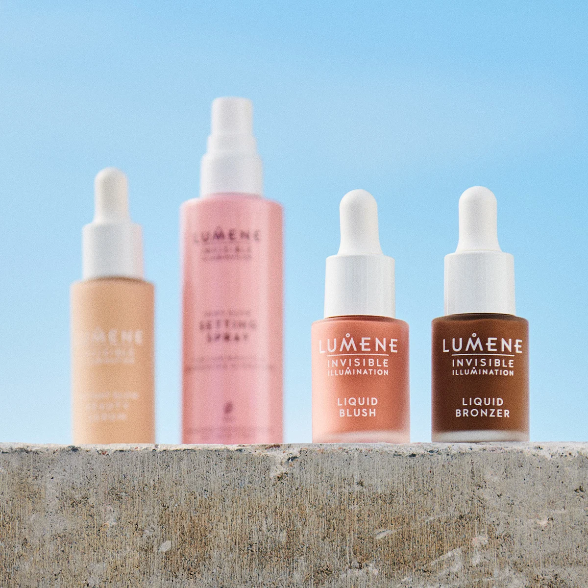 Fire Lumene hudpleieprodukter på en betongoverflate utendørs. Foundation, setting spray, flytende blush og bronzer.