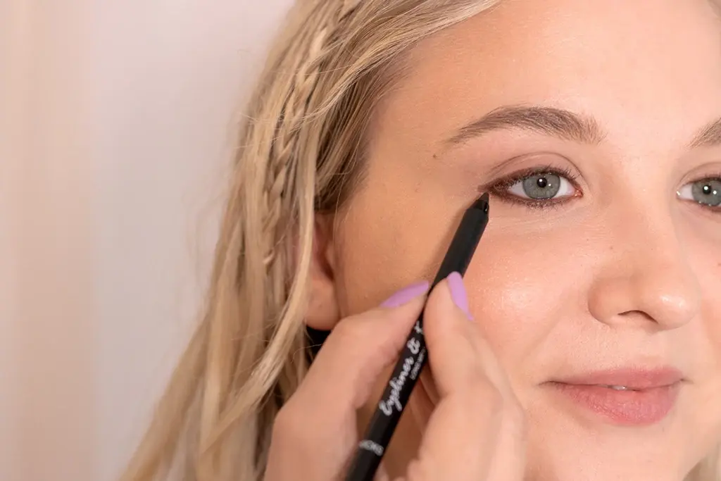 Blond kvinne påfører brun eyelinerstift rundt øyet.