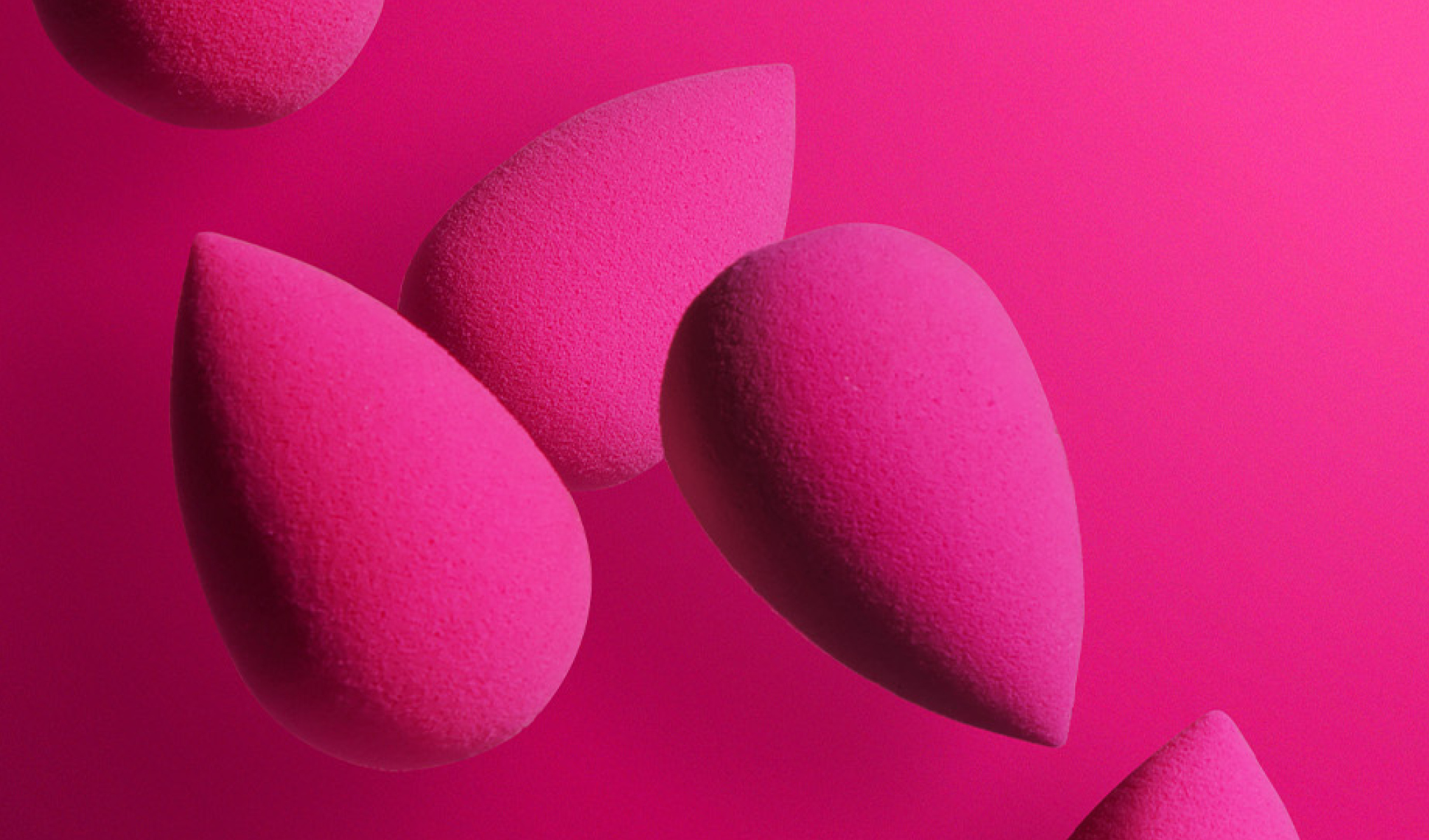 En person med flettet hår holder en rosa sminkesvamp mot ansiktet. Bakgrunnen er knallrosa, som matcher fargen på sminkesvampen. Personen har velstelte negler med lys rosa neglelakk.