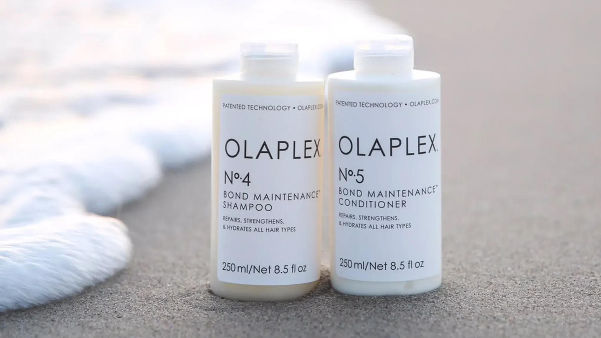 To Olaplex-produkter plassert på en strand ved vannet.