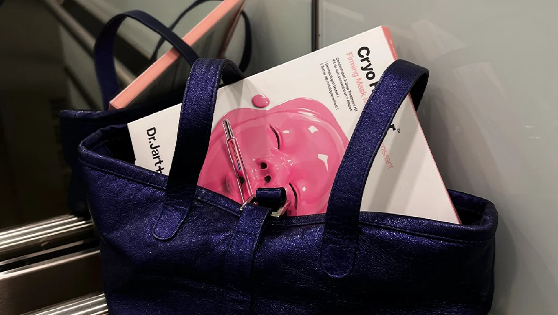 Hohtavan sinisessä laukussa on Dr. Jart+ Cryo Firming Mask -rasia, jossa näkyy vaaleanpunainen kasvonaamio.