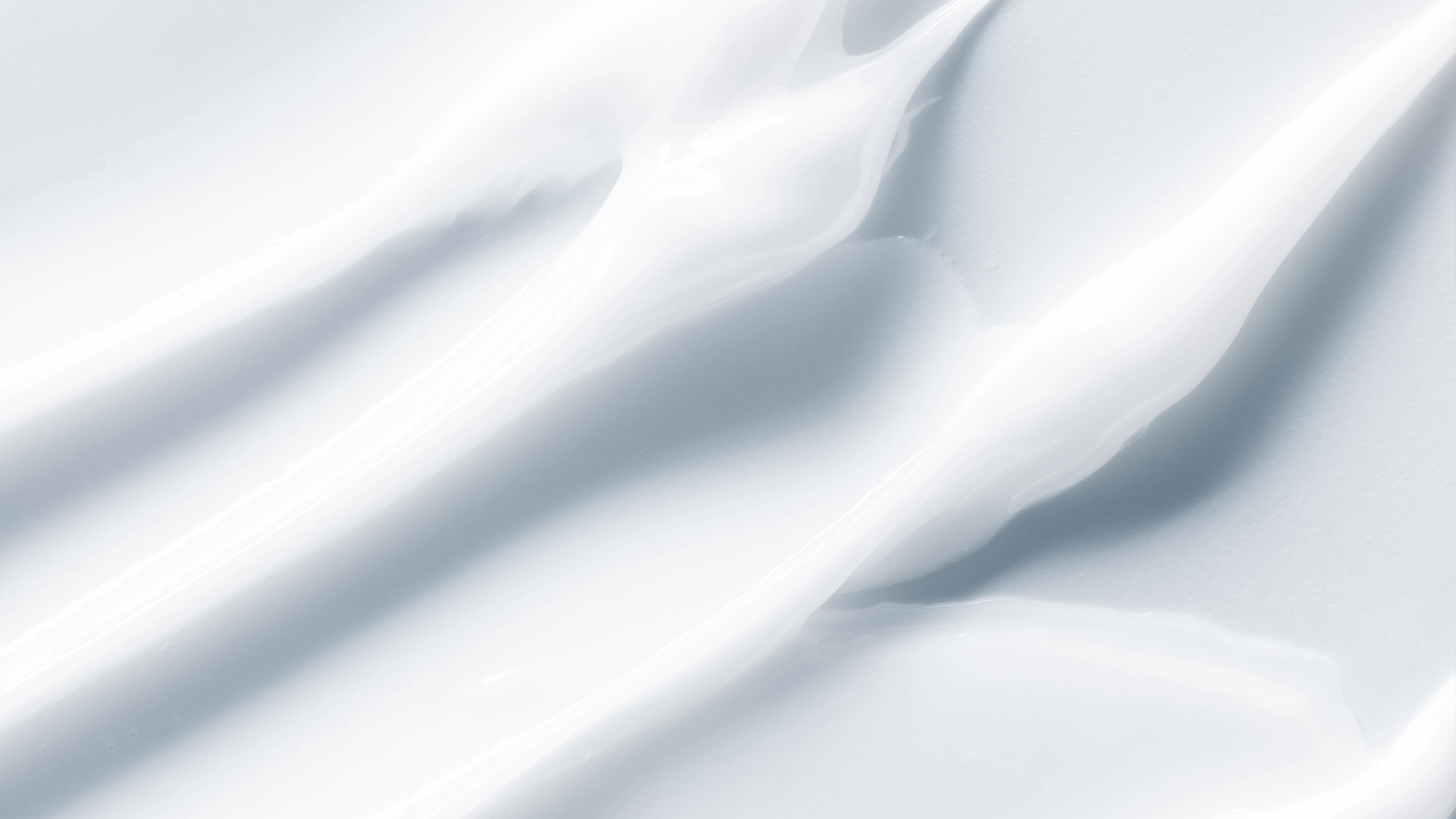 Abstrakt närbild av vit kräm med mjuka, vågformade stråk och slät, krämig textur mot ljus bakgrund.