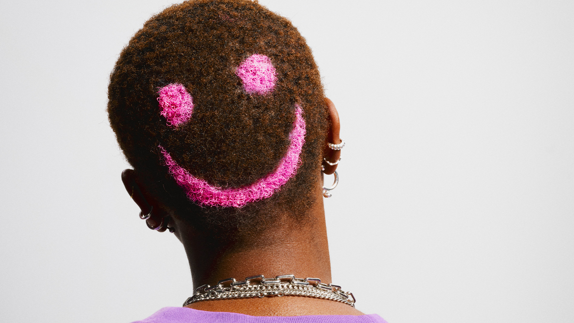 Person med veldig kort hår og et rosa smiley-mønster farget i bakhodet.