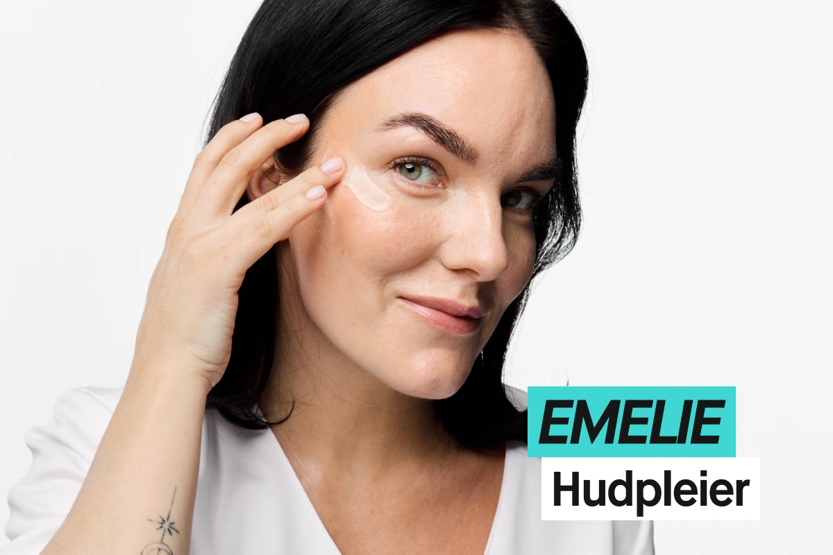 Person med svart hår påfører øyekrem under øyet mot lys grå bakgrunn og har på seg en hvit topp. Turkis og hvit tekst viser “EMELIE” og “Hudterapeut”.