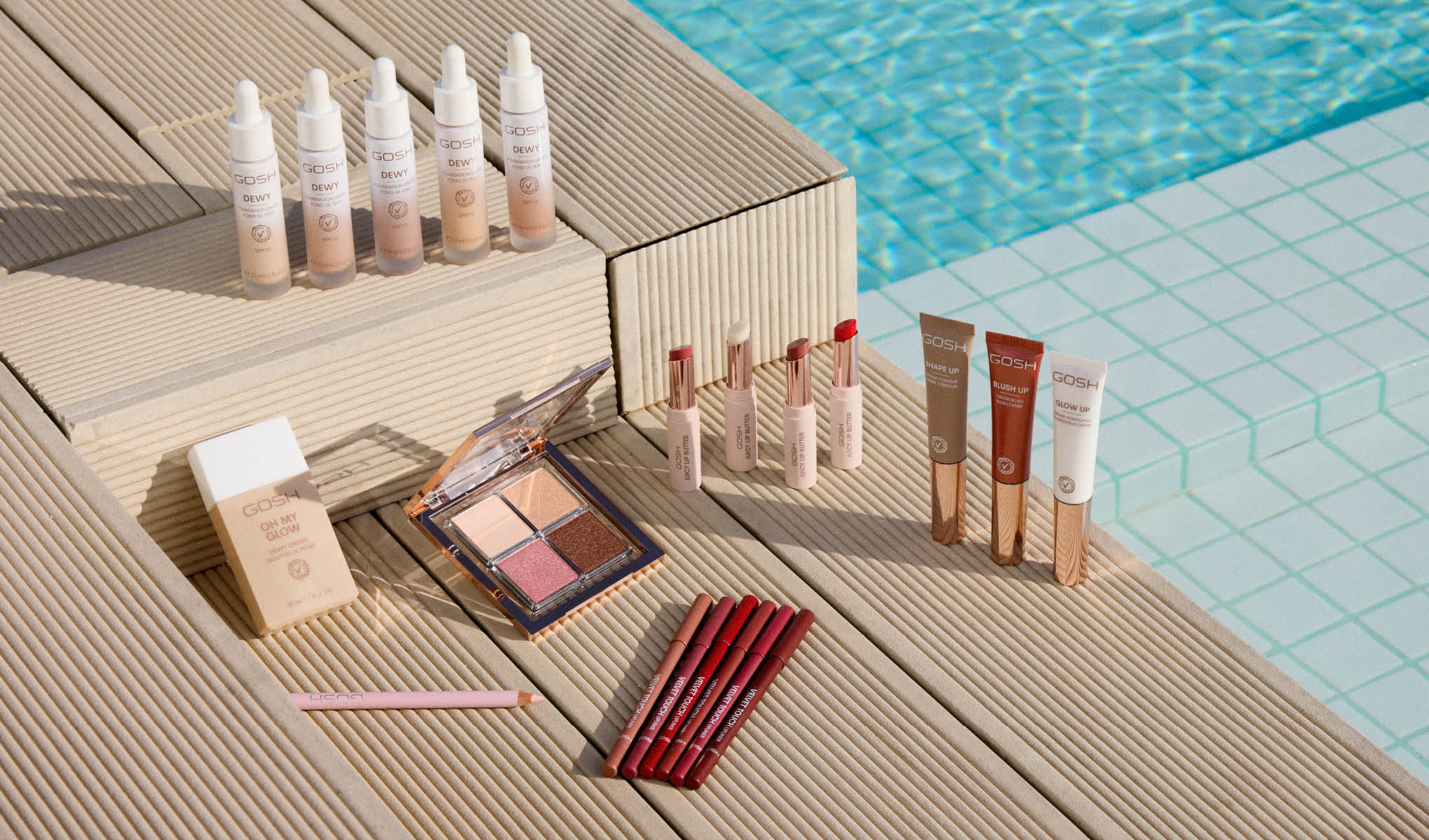 Kosmetikkprodukter plassert ved kanten av et svømmebasseng. Bildet viser forskjellige sminkeprodukter som leppestifter, foundation, concealer og øyenskygger.