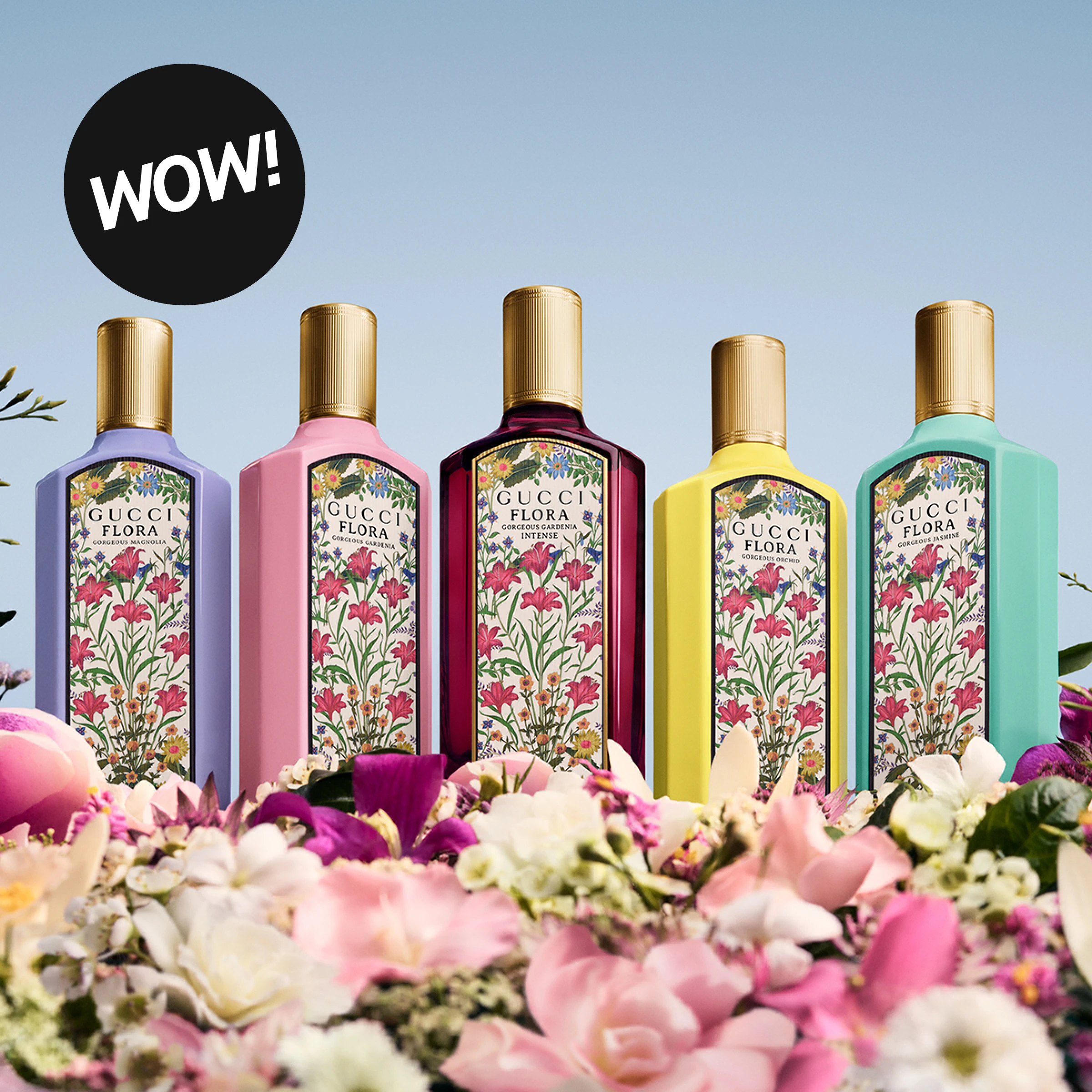 Fem Gucci Flora-parfymer i ulike farger står blant blomster foran en lys blå bakgrunn. Flaskene viser variantene Gorgeous Magnolia, Gorgeous Gardenia, Gorgeous Gardenia Intense, Gorgeous Orchid og Gorgeous Jasmine, og en svart sirkel med teksten “WOW!” vises øverst i bildet.