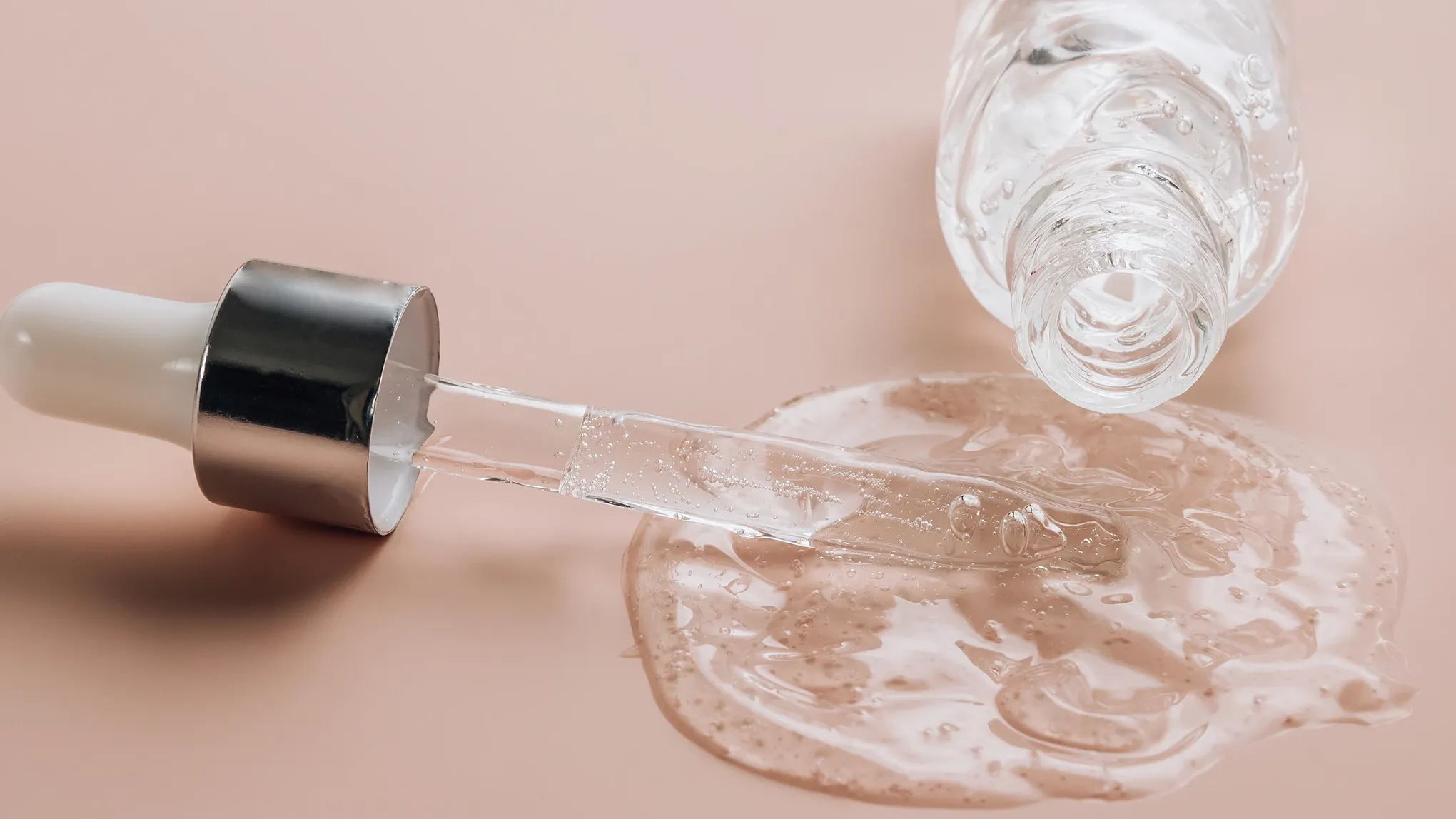 En pipette og en flaske med gjennomsiktig væske som har sølt ut på en beige overflate.