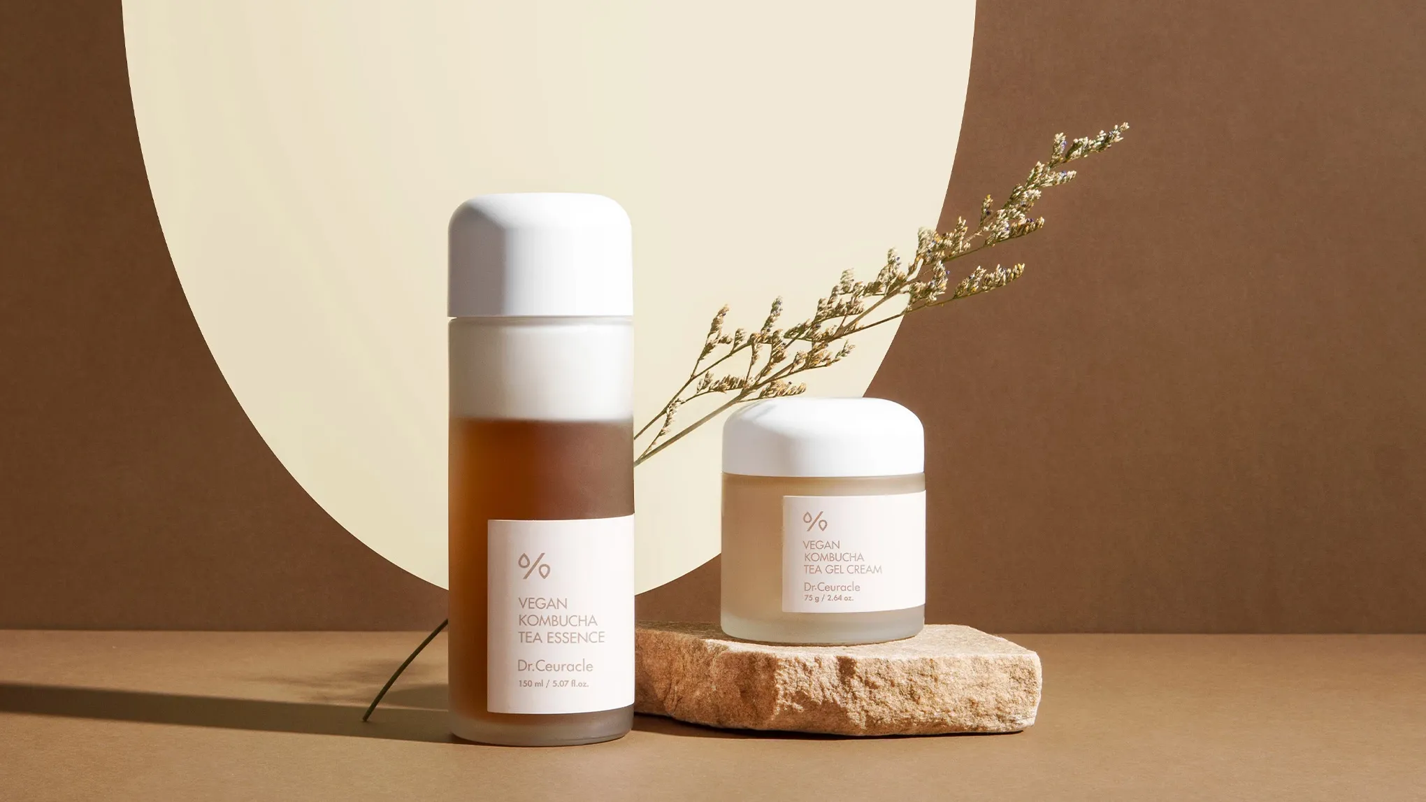 To hudpleieprodukter fra Dr.Ceuracle står plassert mot en beige og brun bakgrunn med en dekorativ plante.