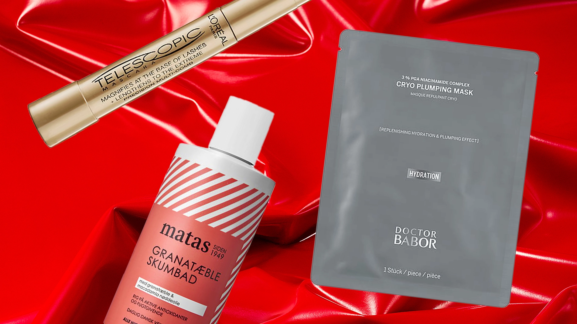Tre skjønnhetsprodukter mot en rød, blank bakgrunn: en gullfarget mascara fra L’Oréal Paris, en grå ansiktsmaske fra Doctor Babor og et rødt granateple-badeskum fra Matas. Rimelige julegavetips innen skjønnhet og hudpleie.