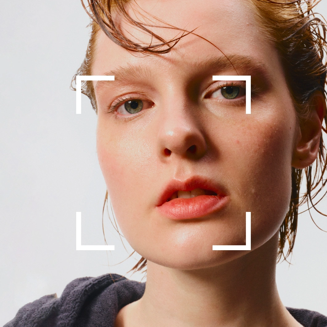 Porträtt av person med fuktig hud och naturlig makeup, inramad av vita markeringar som liknar fokusramar.