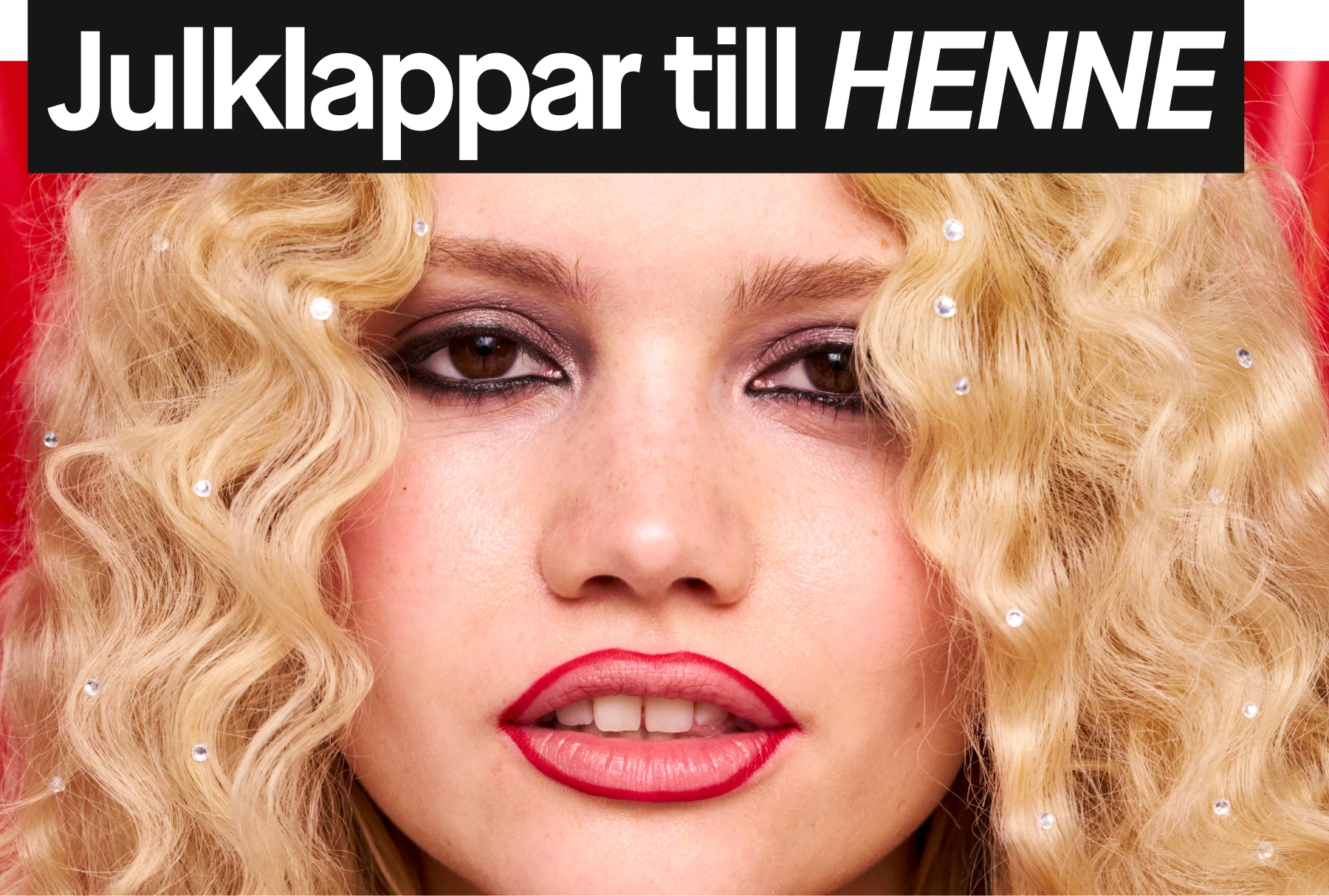 Blont, lockigt hår med dekorativa glittrande detaljer på röd bakgrund.