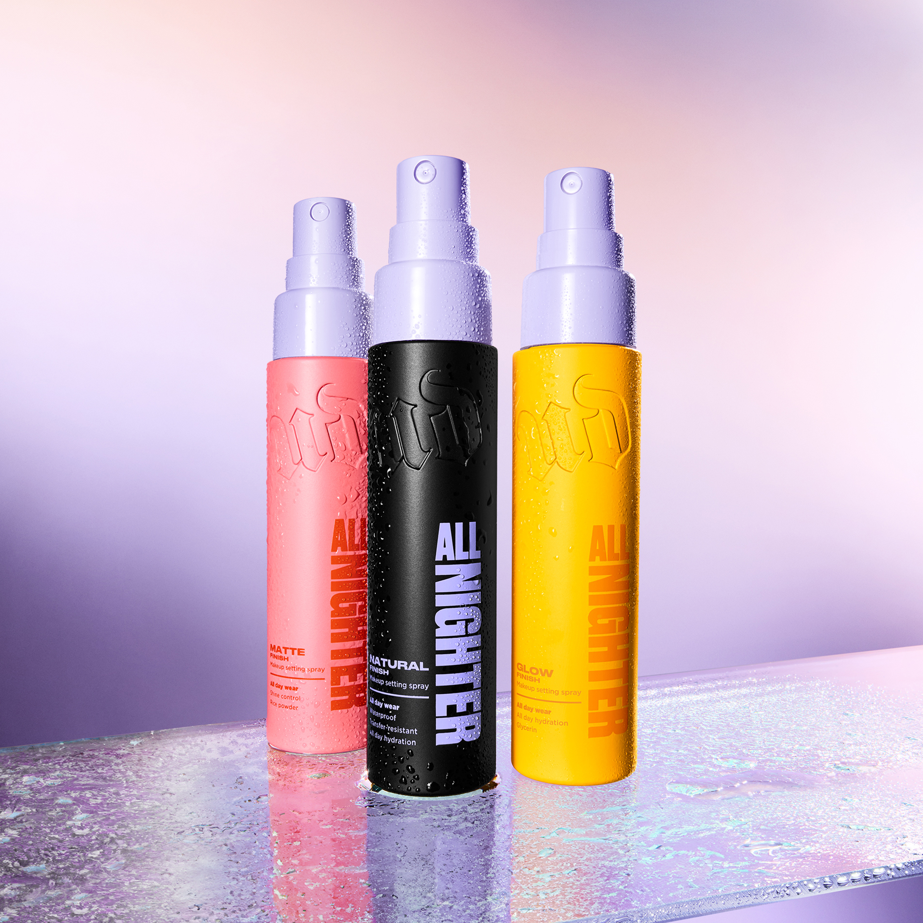 Tre Urban Decay All Nighter setting sprays i rosa, svart og gul flaske med lilla spraypumpe mot lilla bakgrunn. På flaskene vises tekstene “ALL NIGHTER”, “MATTE”, “NATURAL” og “GLOW”.