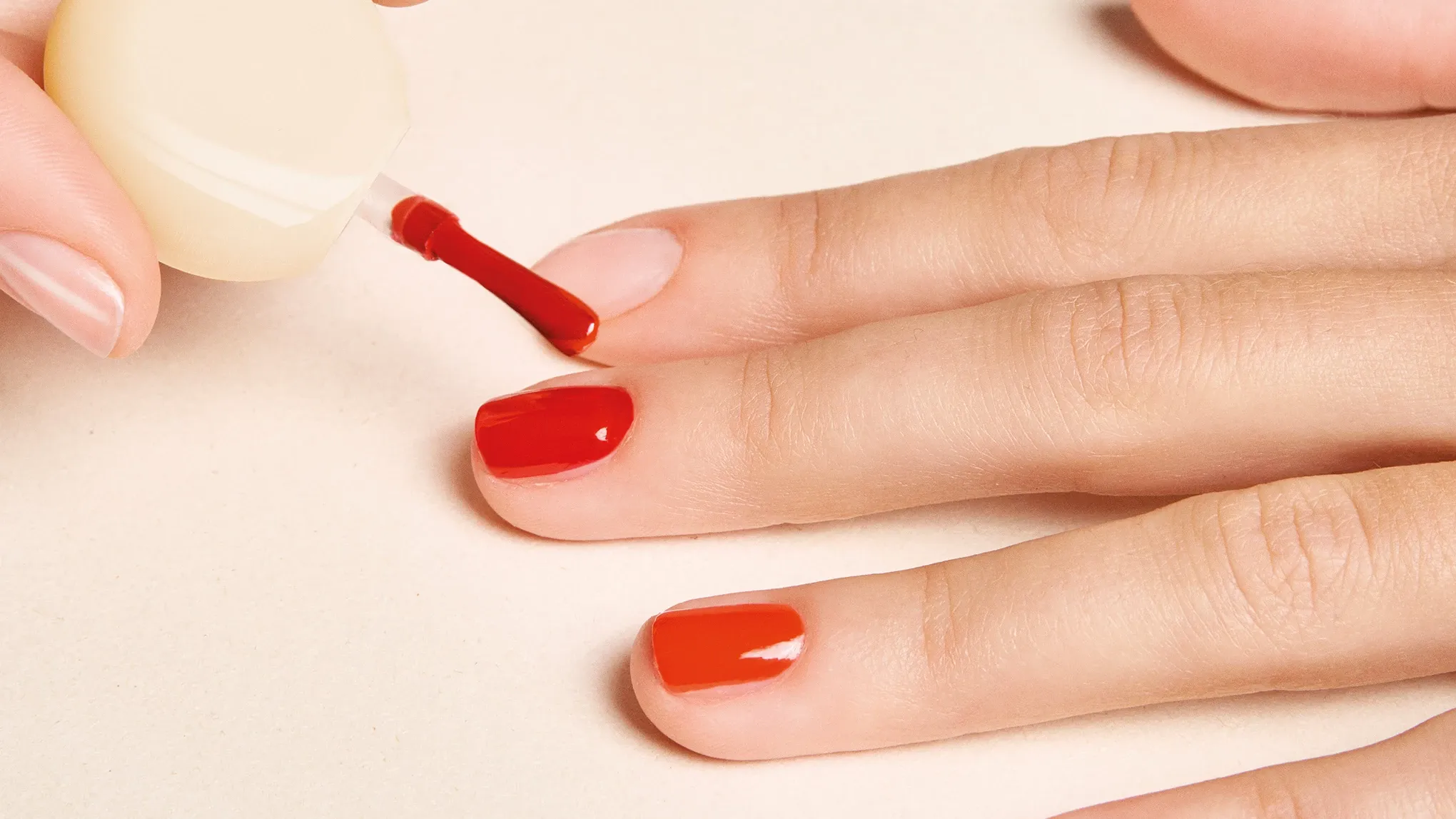Hand som målas med ett rött nagellack mot ett beiget underlag