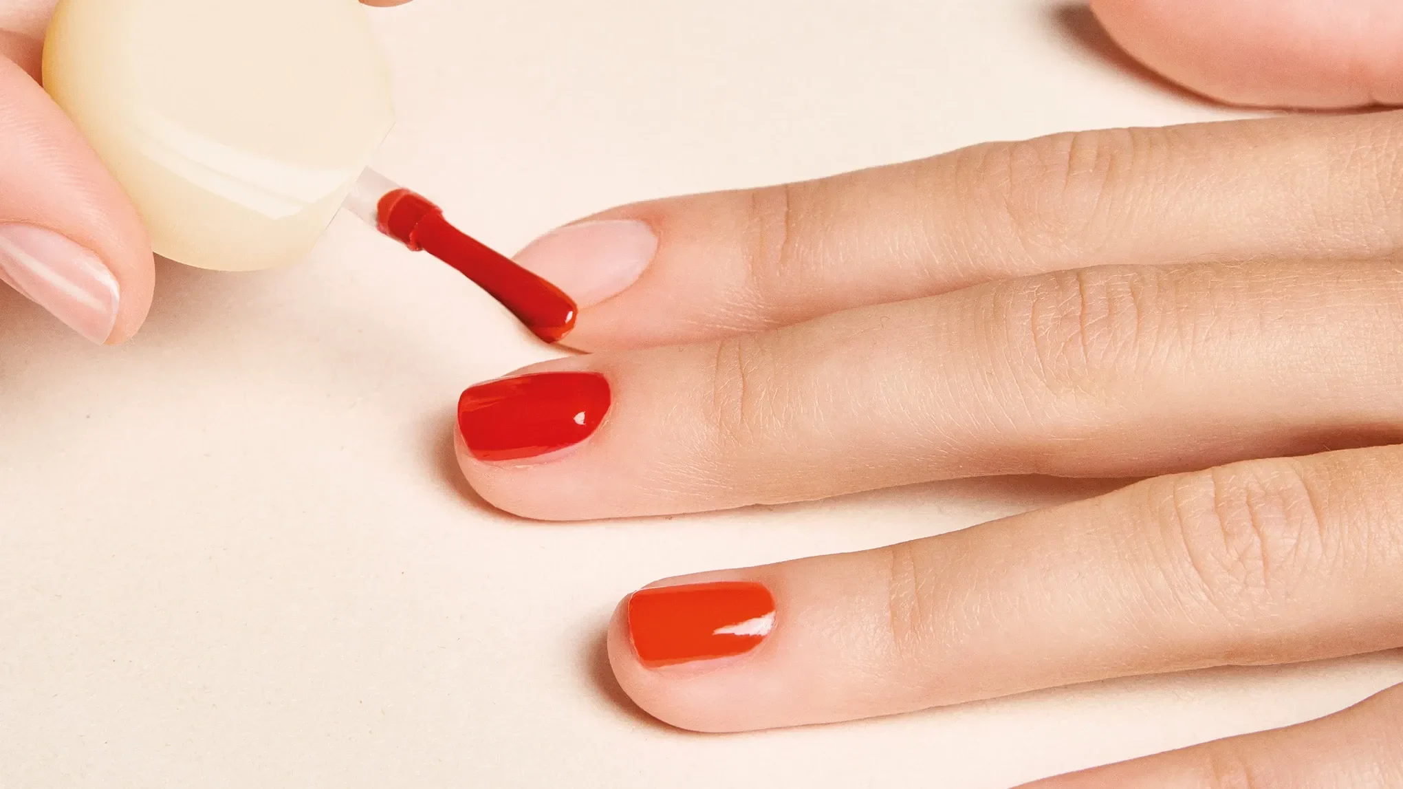 Hand som målas med ett rött nagellack mot ett beiget underlag