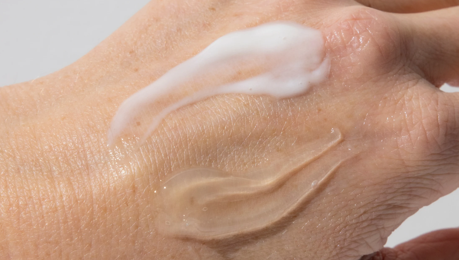 Närbild av två hudvårdsproduktprover på en hand: en vit kräm och en klar, bärnstensfärgad gel.