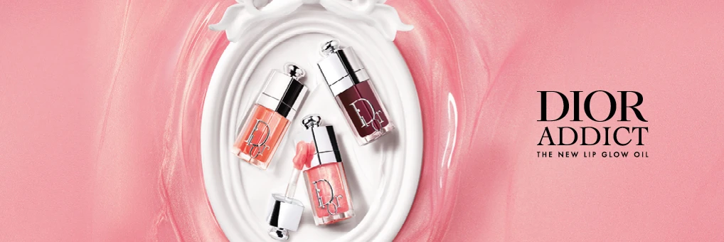 Kolme Dior Addict Lip Glow Oil -huuliöljyä vaaleanpunaisessa, korallin ja tummassa sävyssä hopeisella korkilla valkoisella koristeellisella pinnalla vaaleanpunaisella taustalla. Kuvassa teksti: "DIOR ADDICT" ja "THE NEW LIP GLOW OIL".