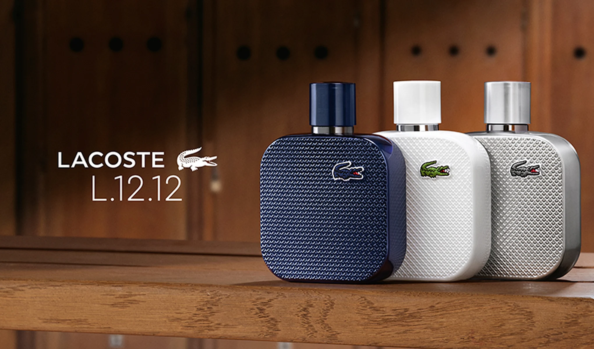 Tre Lacoste L.12.12-parfymeflasker på en treflate i garderobemiljø. Bildet inneholder teksten «Lacoste L.12.12».
