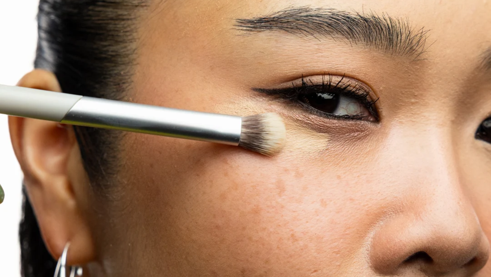 Närbild av en sminkborste som applicerar concealer under en persons öga.
