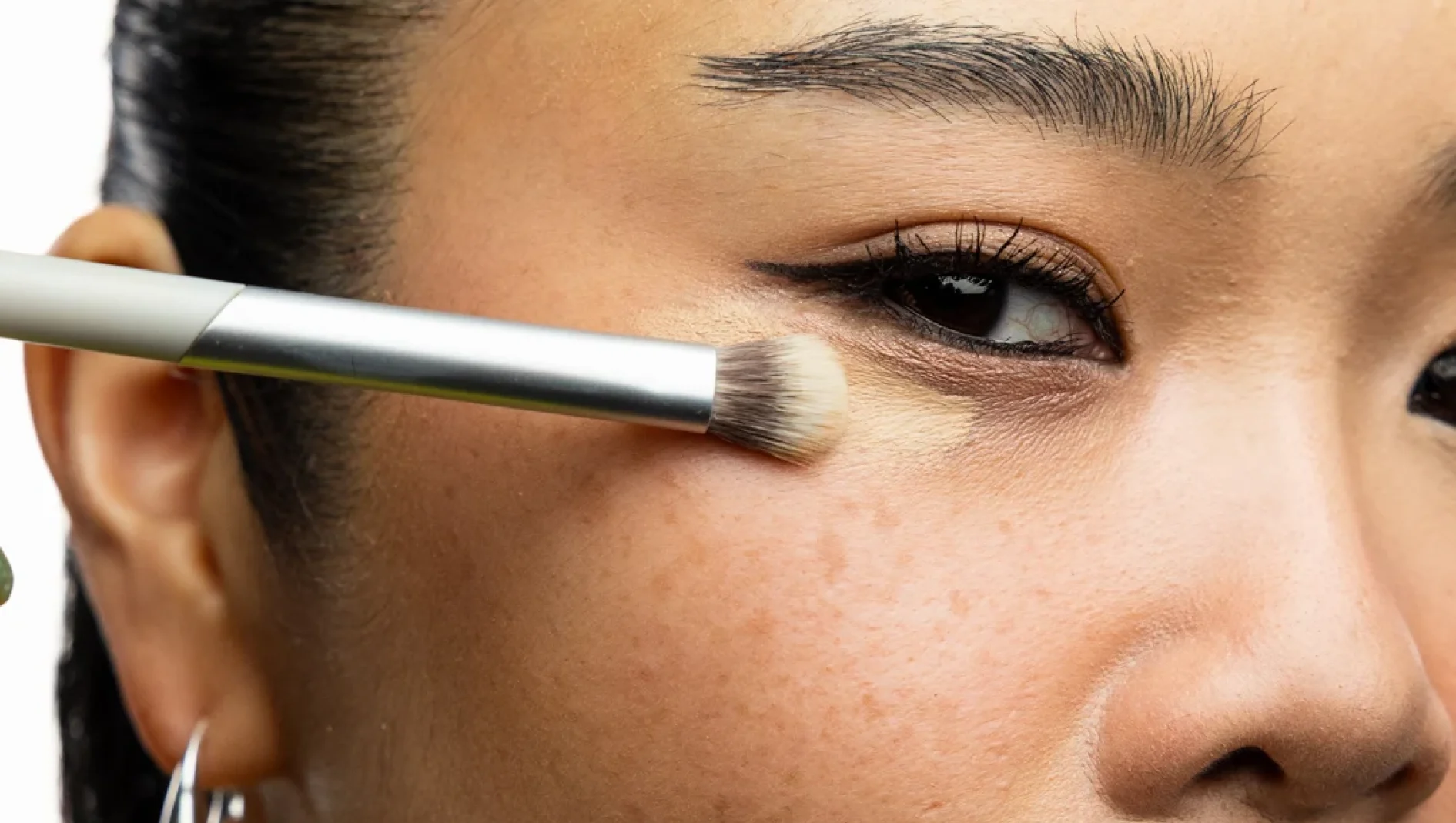 Närbild av en sminkborste som applicerar concealer under en persons öga.