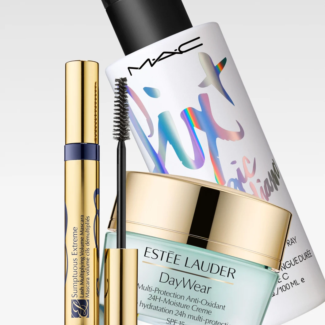 Nærbilde av bestselgere fra Estée Lauder og MAC Cosmetics: Estée Lauder DayWear Multi-Protection Anti-Oxidant 24H-Moisture Creme SPF 15, Estée Lauder Sumptuous Extreme Lash Multiplying Volume Mascara med synlig mascarabørste og MAC Fix+ Magic Radiance. Produktene vises mot en lys grå bakgrunn med synlige produktnavn og produkttekster.