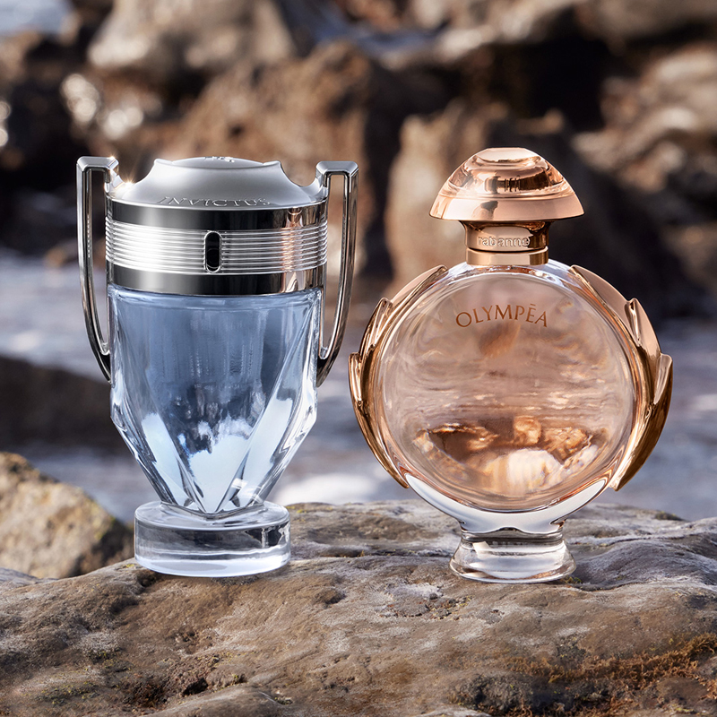 Rabanne Invictus- ja Olympéa-tuoksut. Kaksi pulloa kivellä ulkona; vasemmalla hopeinen Invictus, oikealla vaaleanpunainen Olympéa.