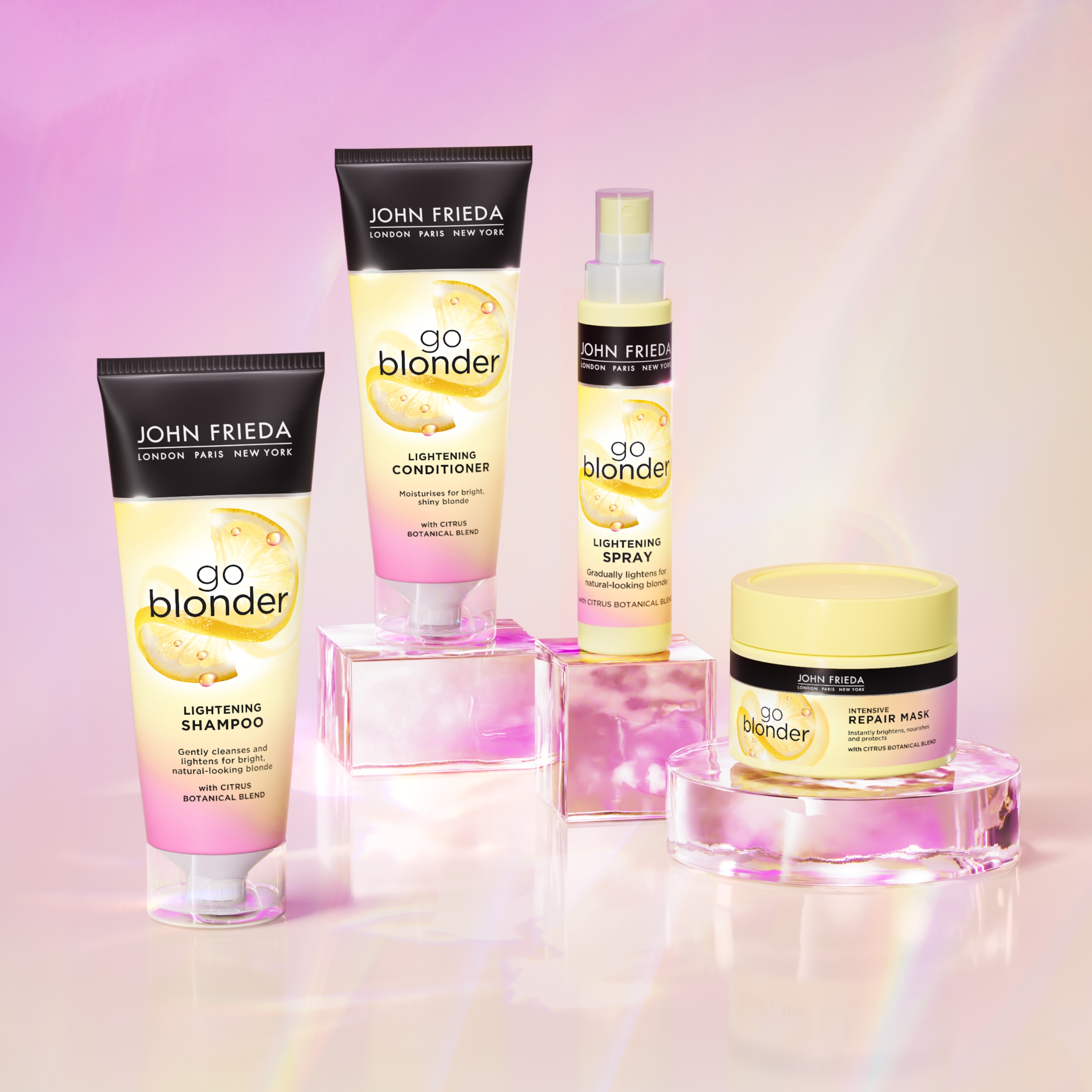 Neljä John Frieda Go Blonder -tuotetta vaaleanpunaisen ja keltaisen taustan edessä. Kuvassa on shampoo, hoitoaine, suihke ja korjaava hiusnaamio.