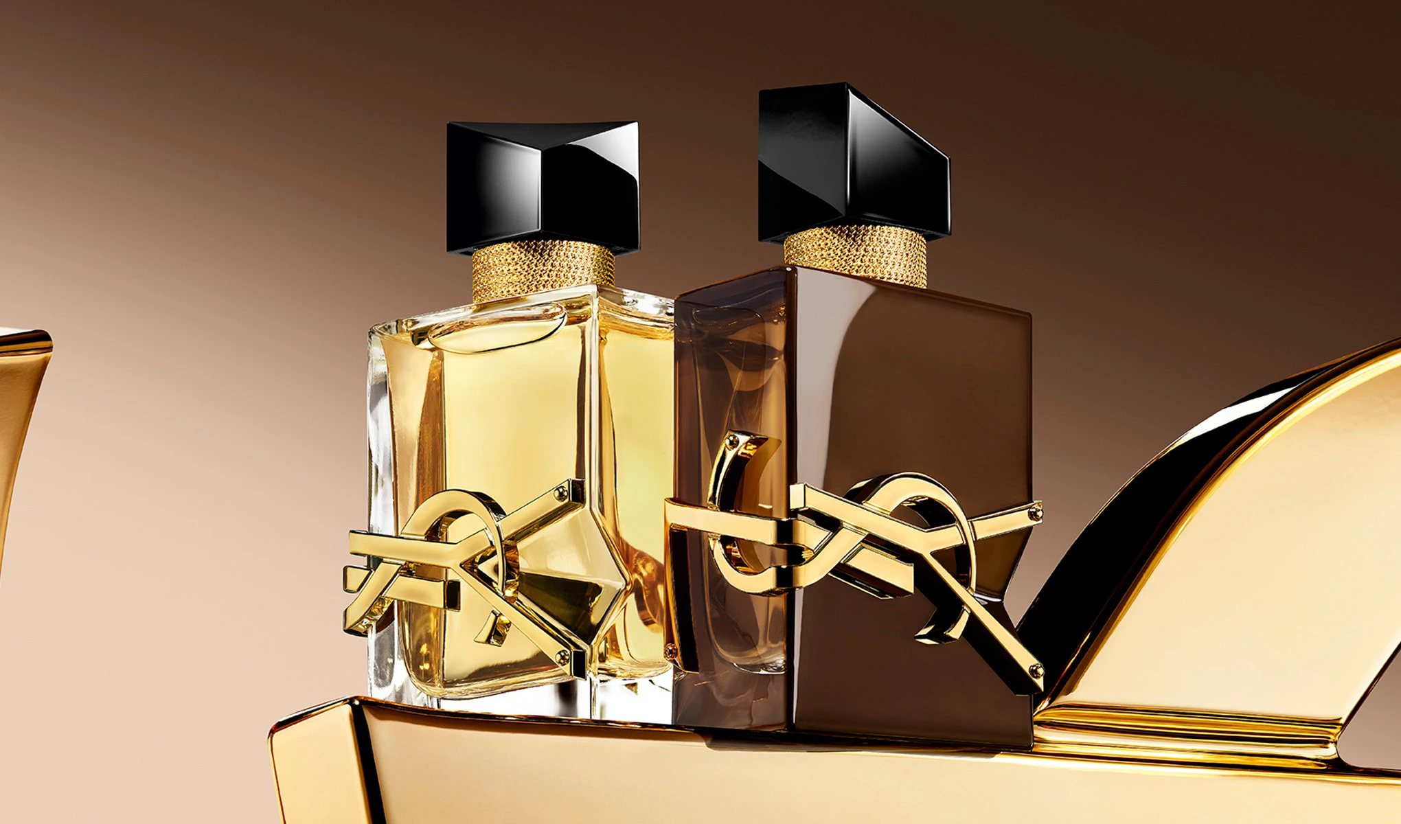 To YSL-parfymeflasker: en lys og en mørk, begge med gullogoer og svarte korker på en gyllen overflate.