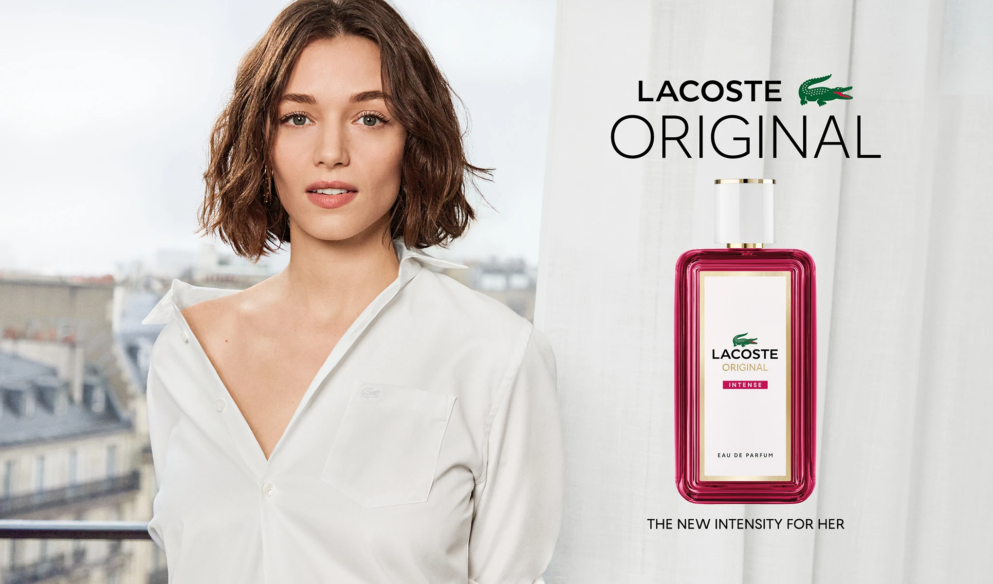 Nainen valkoisessa paidassa ja Lacoste Original Intense -tuoksupullo. Teksti: ”Lacoste Original. The new intensity for her.”