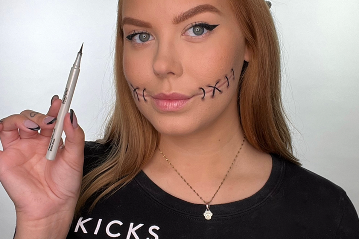 Nainen, jolla on tikkimäinen meikki poskissa, kädessään eyeliner-kynä.