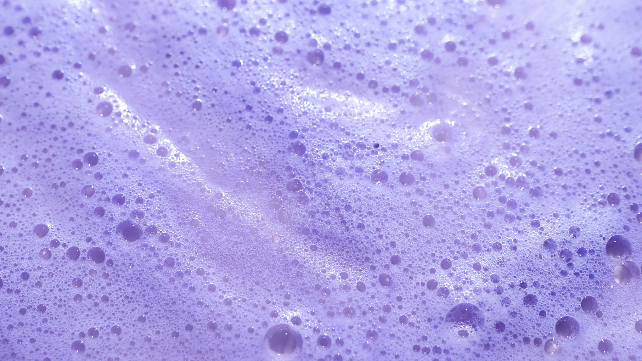Lähikuva violetista vaahdosta ja kuplista, todennäköisesti sävyttävästä shampoosta.